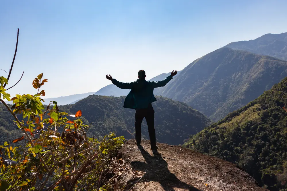 A man stood with arms in the air around mountains after completing the Thrive Inside Online Meditation Course.